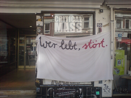 Ein Transparent mit der Aufschrift "Wer lebt, stört", an einer Geschäftsfassade